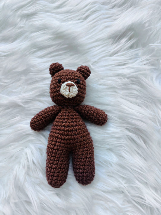 Handmade brown crochet teddy bear lying on white fluffy surface - mini stuffed animal toy, 4-5 inches tall