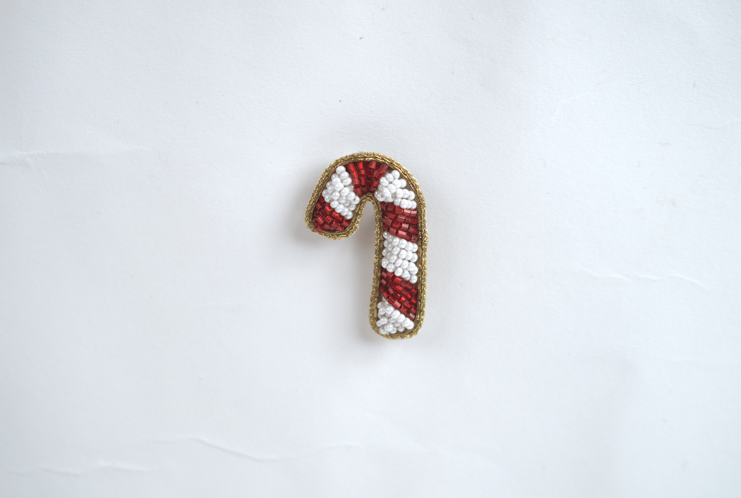 Handmade beaded candy cane hair clip with red and white beads and gold border – top view on white background