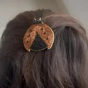 Handcrafted ladybug hair clip worn in dark hair, showing orange and black beaded design