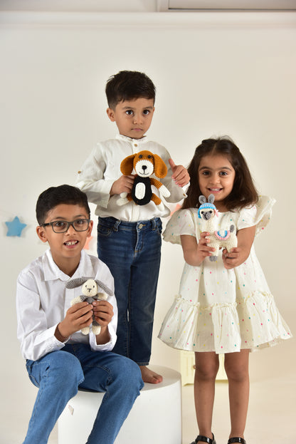 Three children in matching outfits displaying handmade crochet bunny and animal stuffed toys