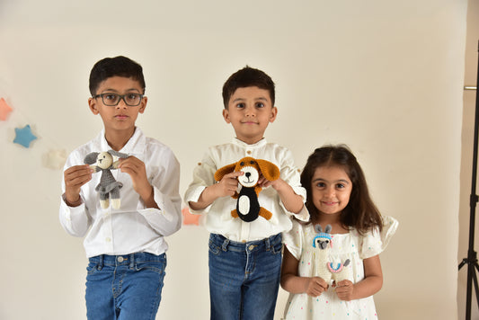 Three children holding handmade crochet stuffed toys including a bunny rabbit and other animals