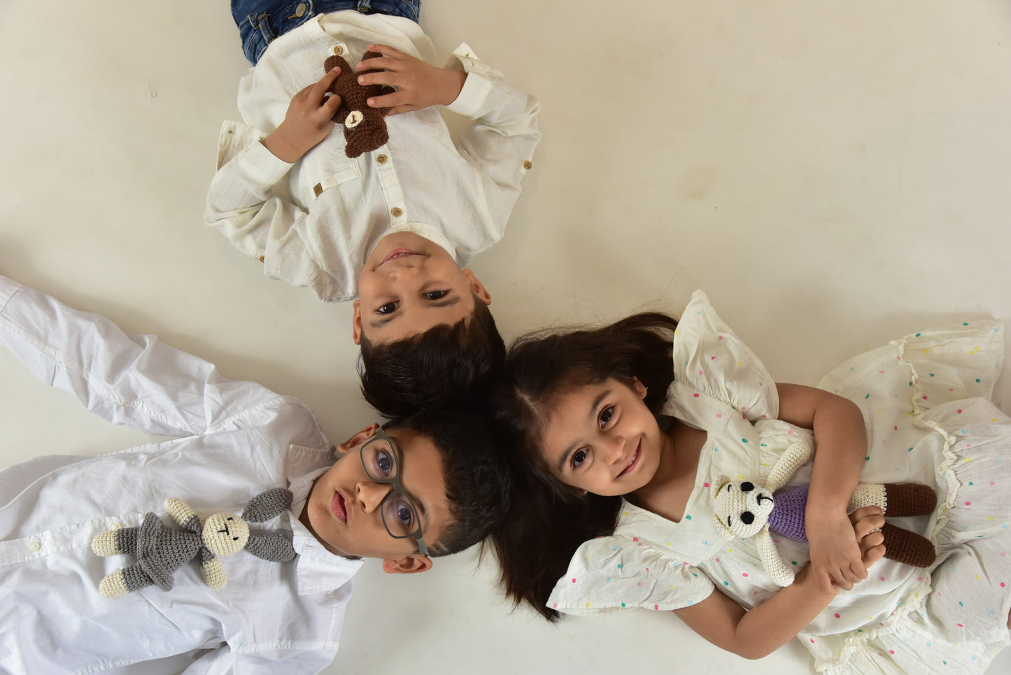 Three children lying down holding handmade crochet teddy bear stuffed toys, showcasing the perfect cuddly companion for kids of all ages