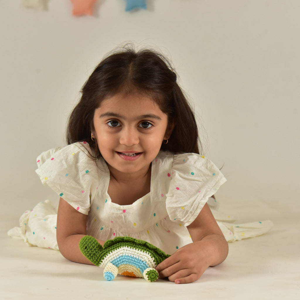 Young girl smiling while holding a small handmade green crochet dinosaur toy