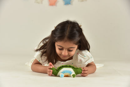Child lying down and playing with a small handmade green crochet dinosaur toy