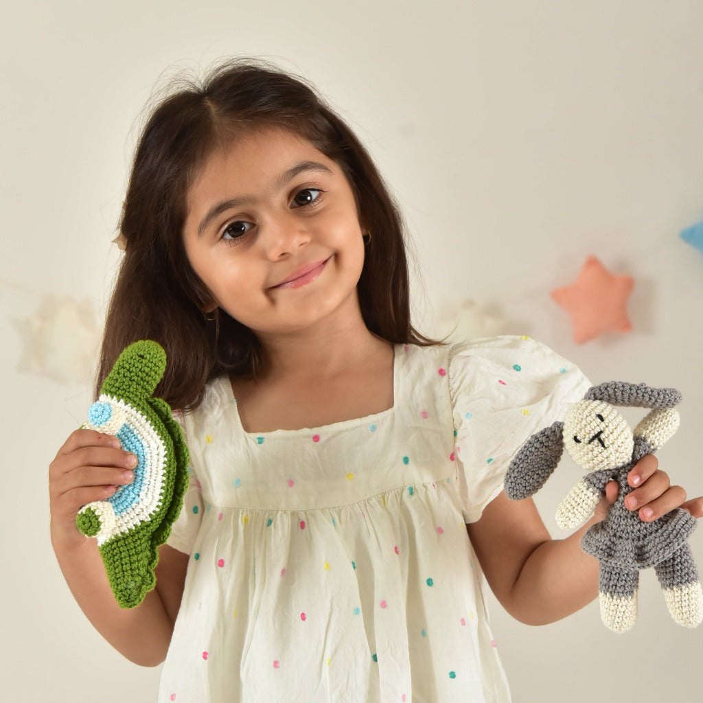 Girl in white dress holding handmade crochet bunny and dinosaur toys with star decorations background