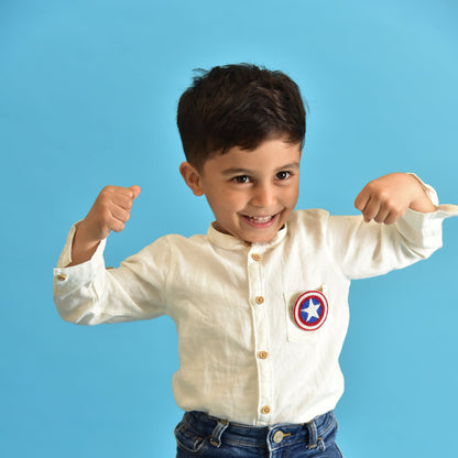 Young boy wearing Captain America beaded shield brooch on white shirt, smiling against blue background