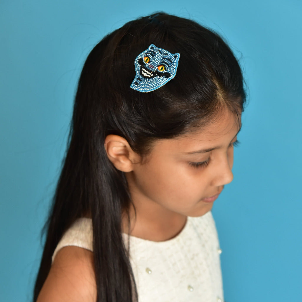 Young girl wearing blue beaded Derpy Tiger hair clip in white dress against blue background