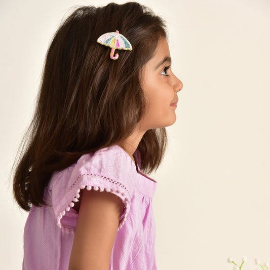 Young girl wearing Monsoon Muse multicolor beaded umbrella hair clip, side profile in pink dress