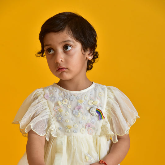 Child in a white dress with colourful accents wearing a cloud brooch. 