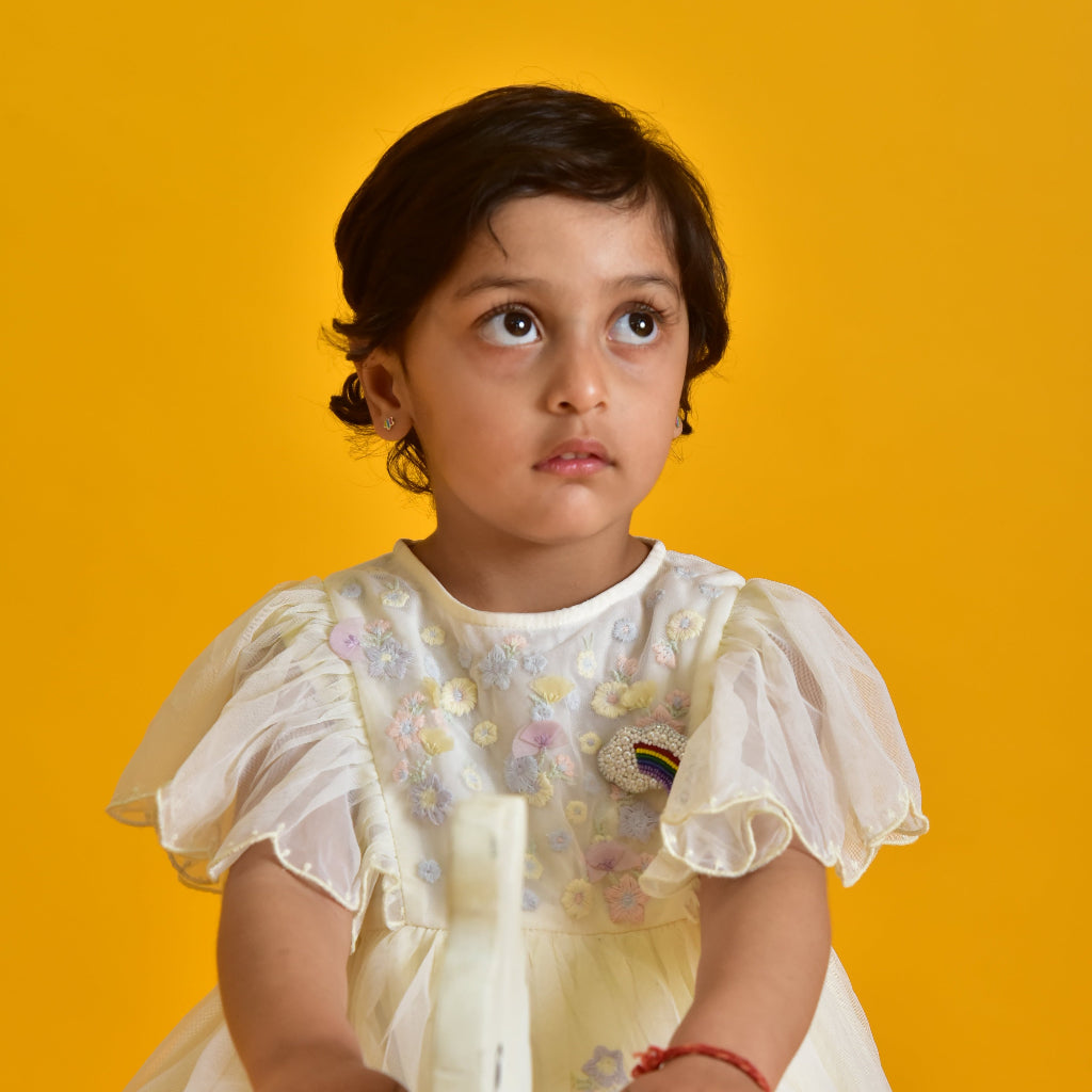 Young girl wearing a white dress with a rainbow cloud Brooch