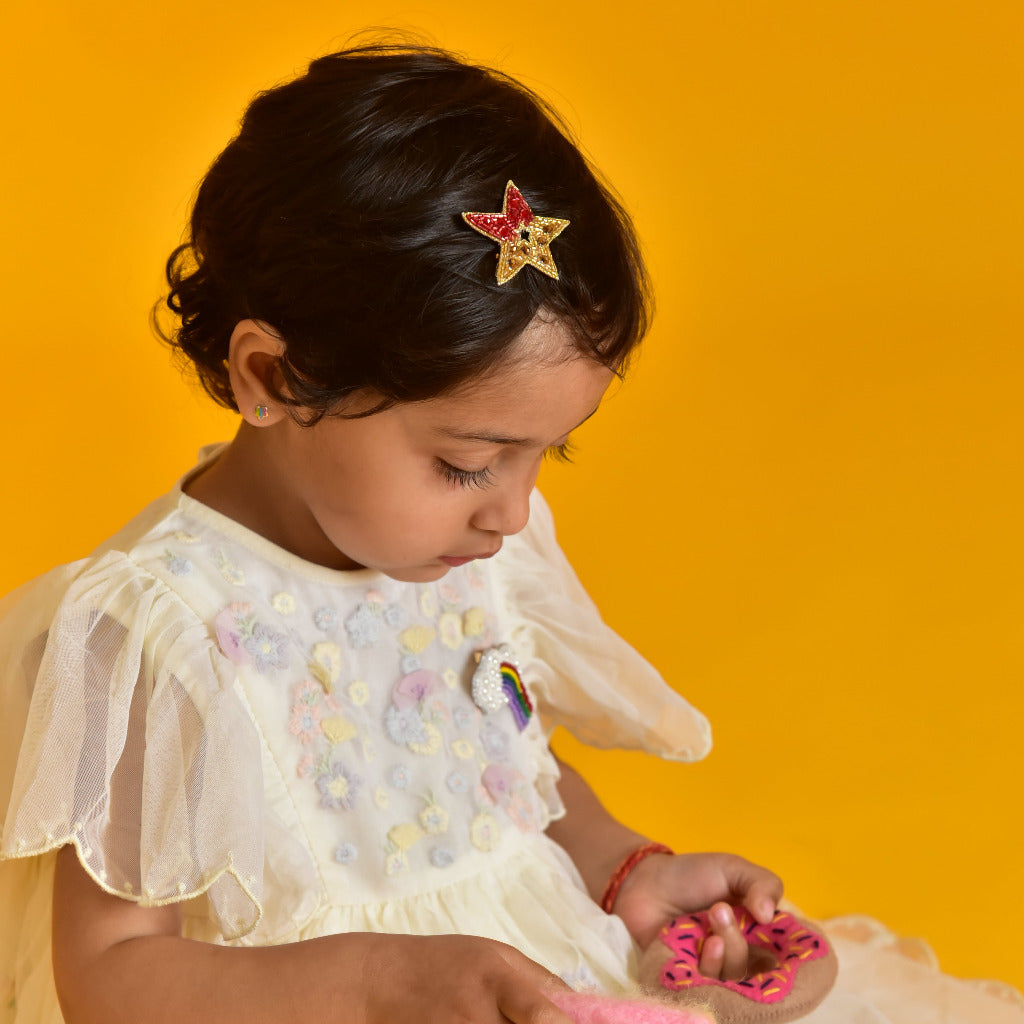 Young girl wearing red beaded Guiding Star Hair Clip in white dress against yellow background
