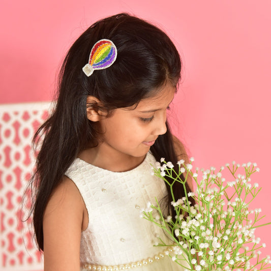 Young girl wearing handmade rainbow hot air balloon hair clip in white dress on pink background