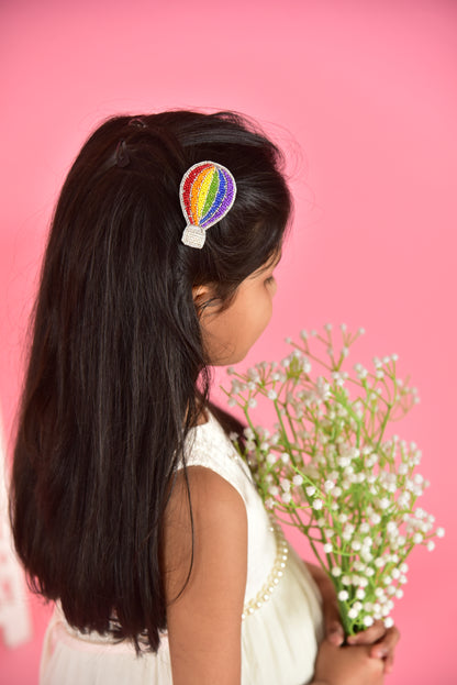Side profile of girl wearing rainbow hot air balloon hair clip with flowers on pink background