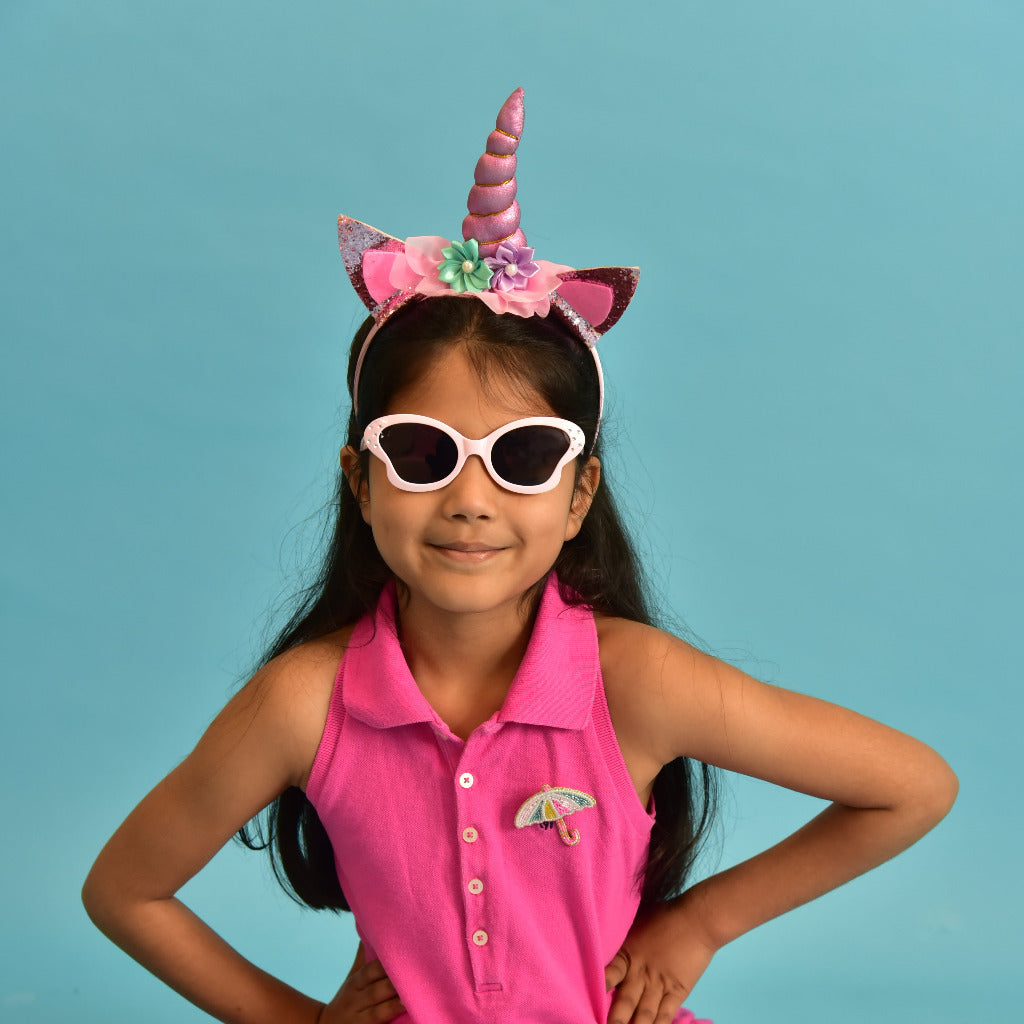 Young girl wearing a pink unicorn headband and sunglasses against a blue background