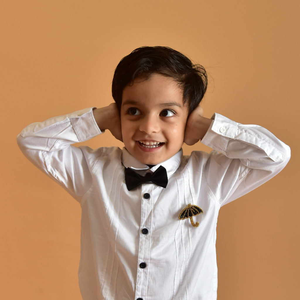 Child wearing a white shirt with black buttons and a black bow tie, standing against a beige background.
