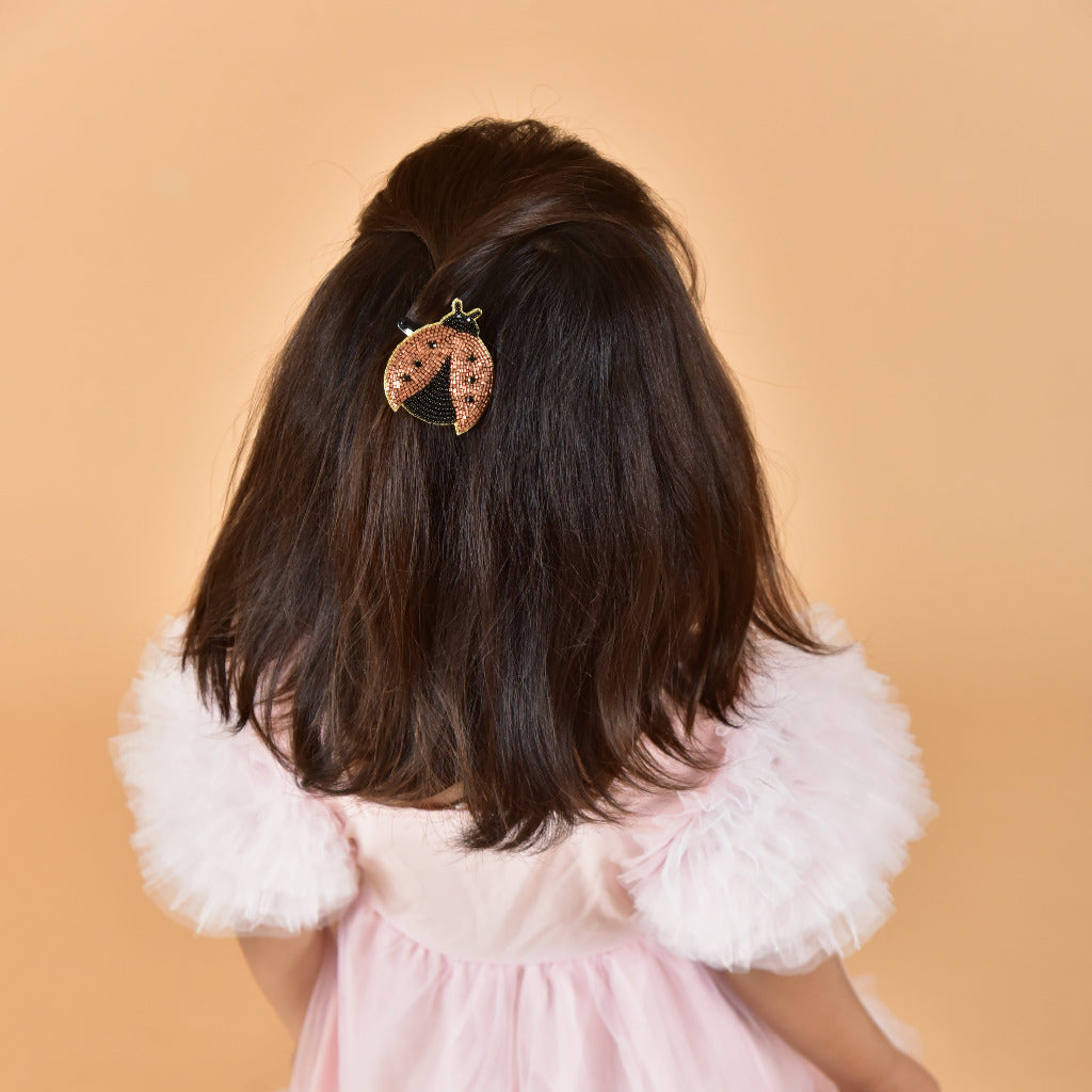 Young girl in pink dress wearing ladybug hair clip in dark hair, back view showing styled look