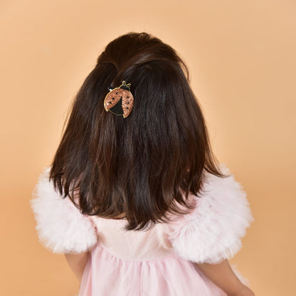 Young girl in pink dress wearing ladybug hair clip in dark hair, back view showing styled look