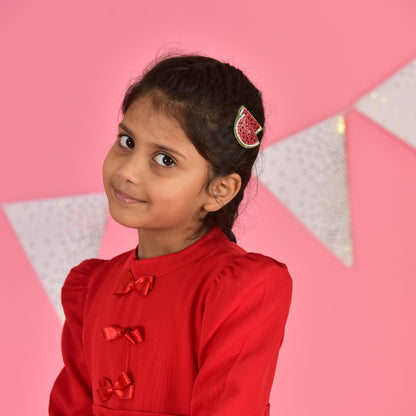 Girl in red outfit wearing a handmade watermelon hair clip, looking over her shoulder on a pink background