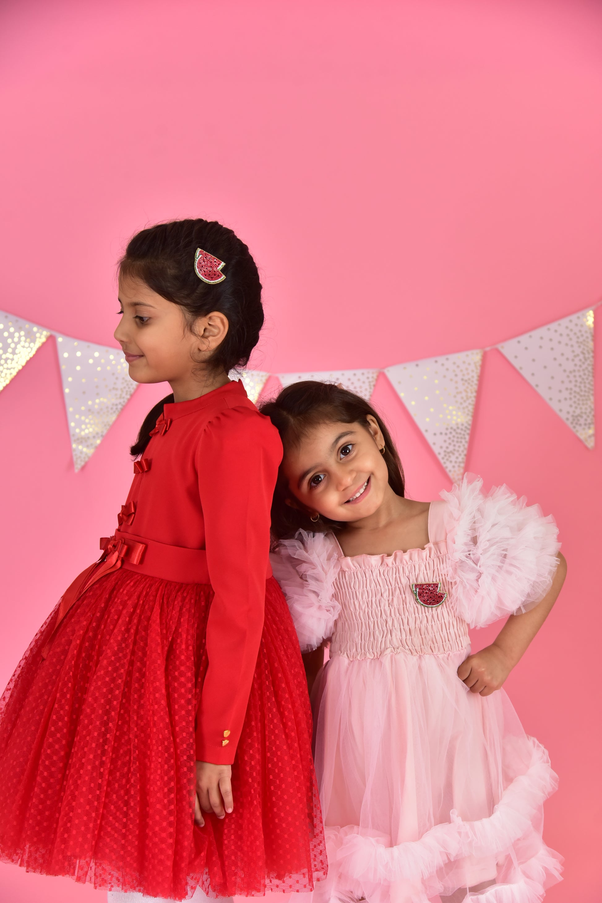 Two girls in festive dresses on pink background, one wearing a handmade watermelon hair clip by Little Pink Llama
