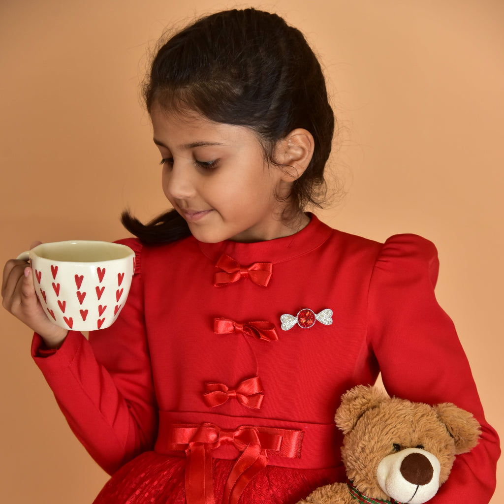Young girl in red dress wearing Little Pink Llama candy brooch pin holding mug and teddy bear
