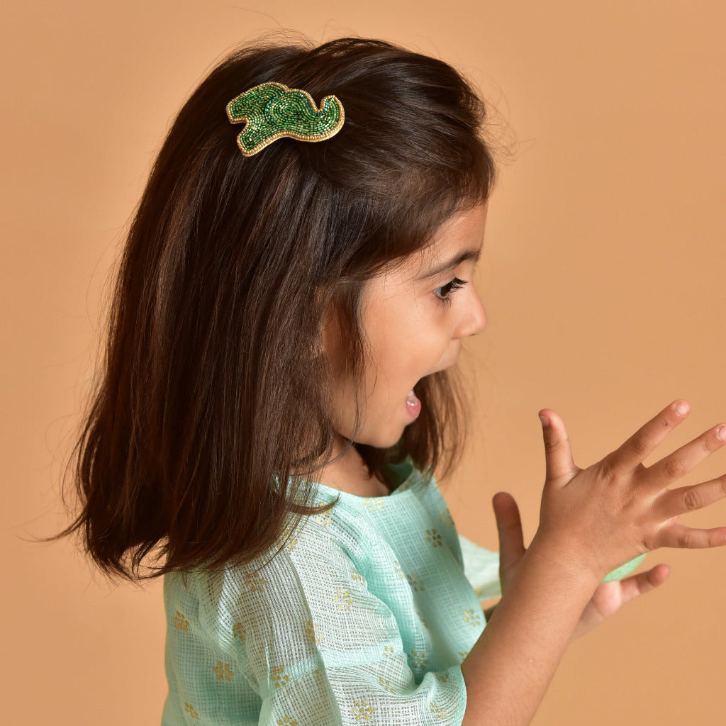 Young girl in teal dress wearing green beaded elephant hair clip - handmade kids hair accessory on beige background
