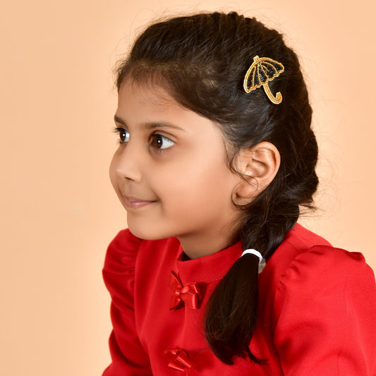 Young girl wearing Monsoon Muse black beaded umbrella hair clip in red outfit, side profile
