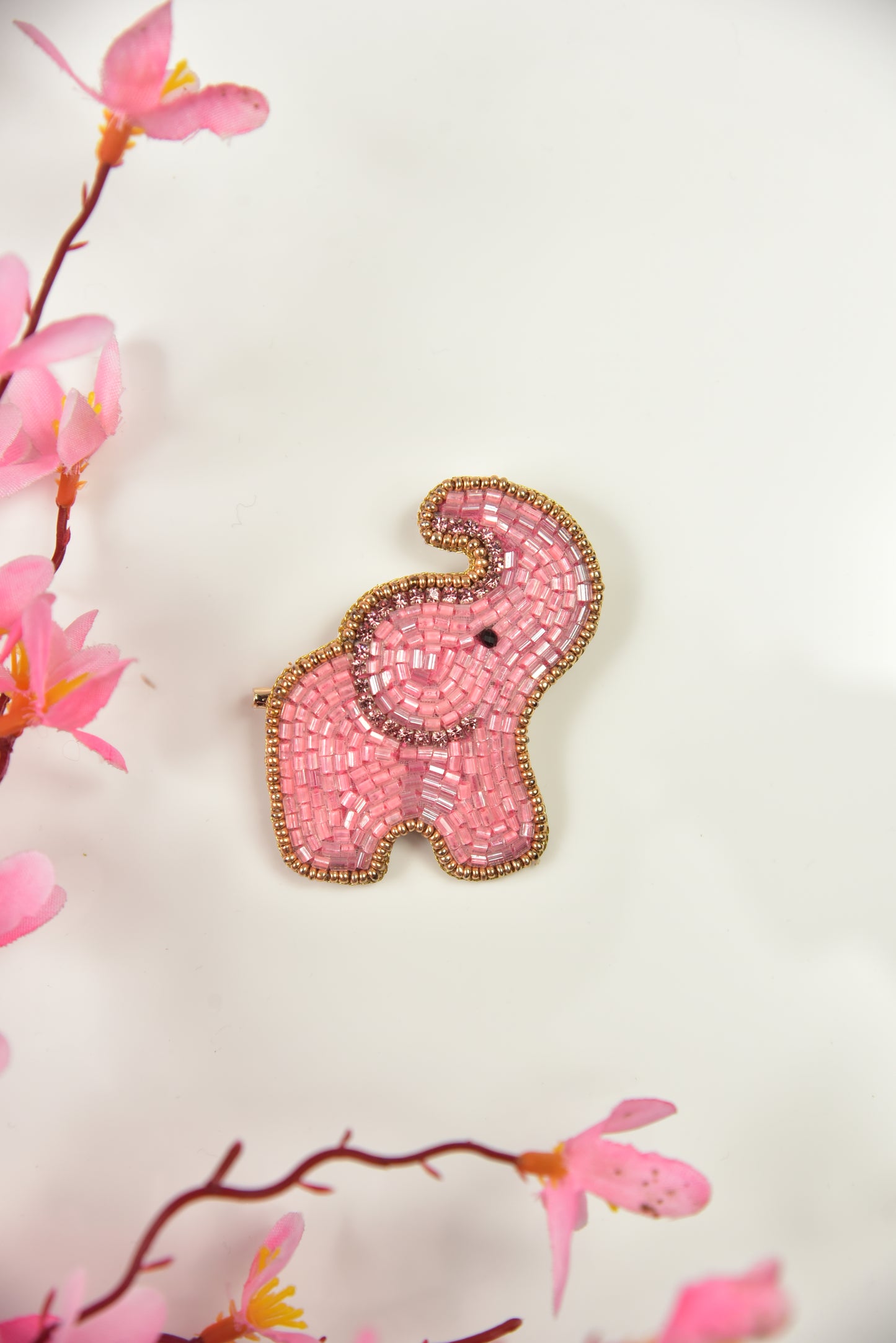 Pink handcrafted beaded elephant brooch with gold border against floral background—kids jewelry by Little Pink Llama