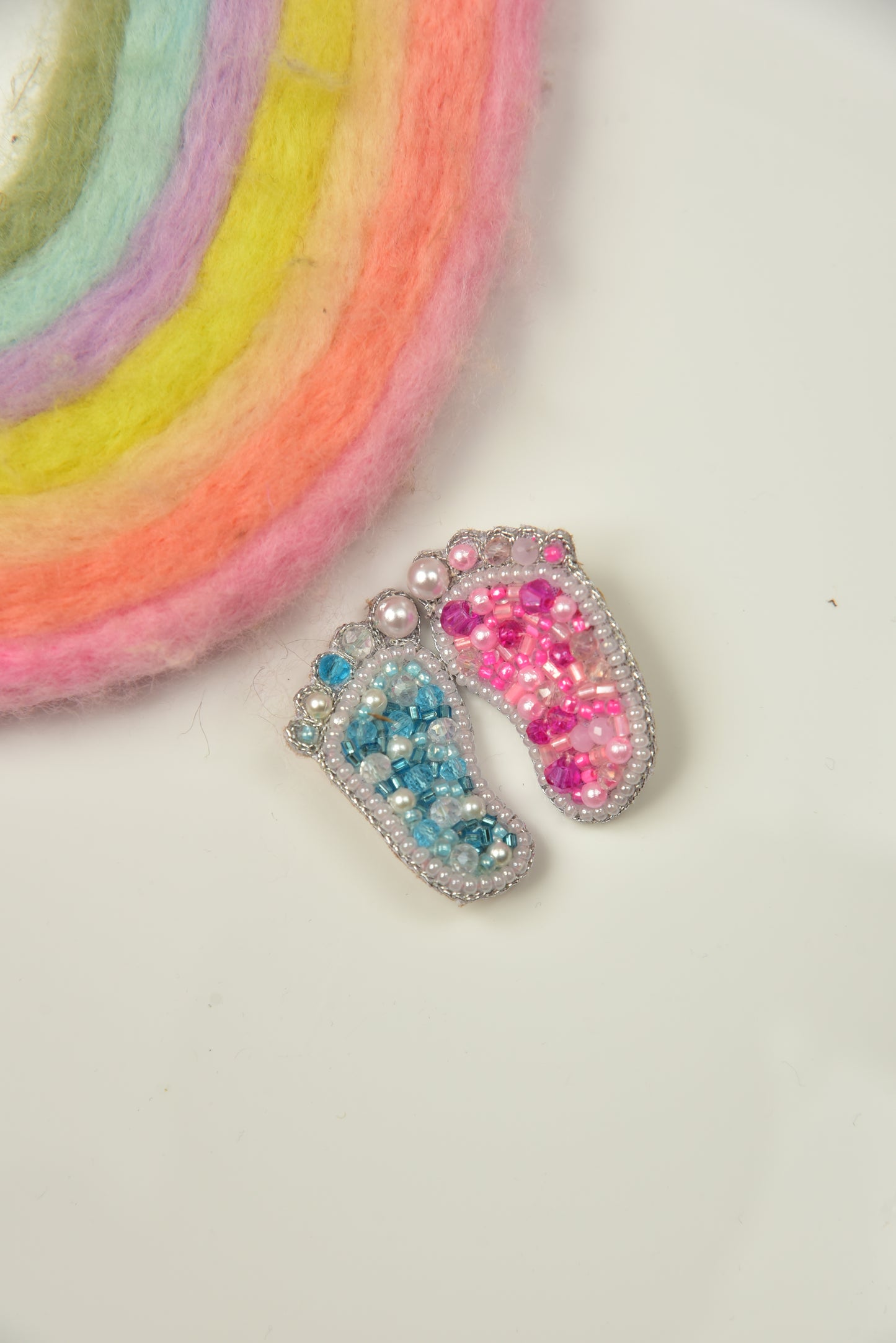 Blue and pink handcrafted baby feet brooches styled with rainbow prop—gender reveal gift set by Little Pink Llama