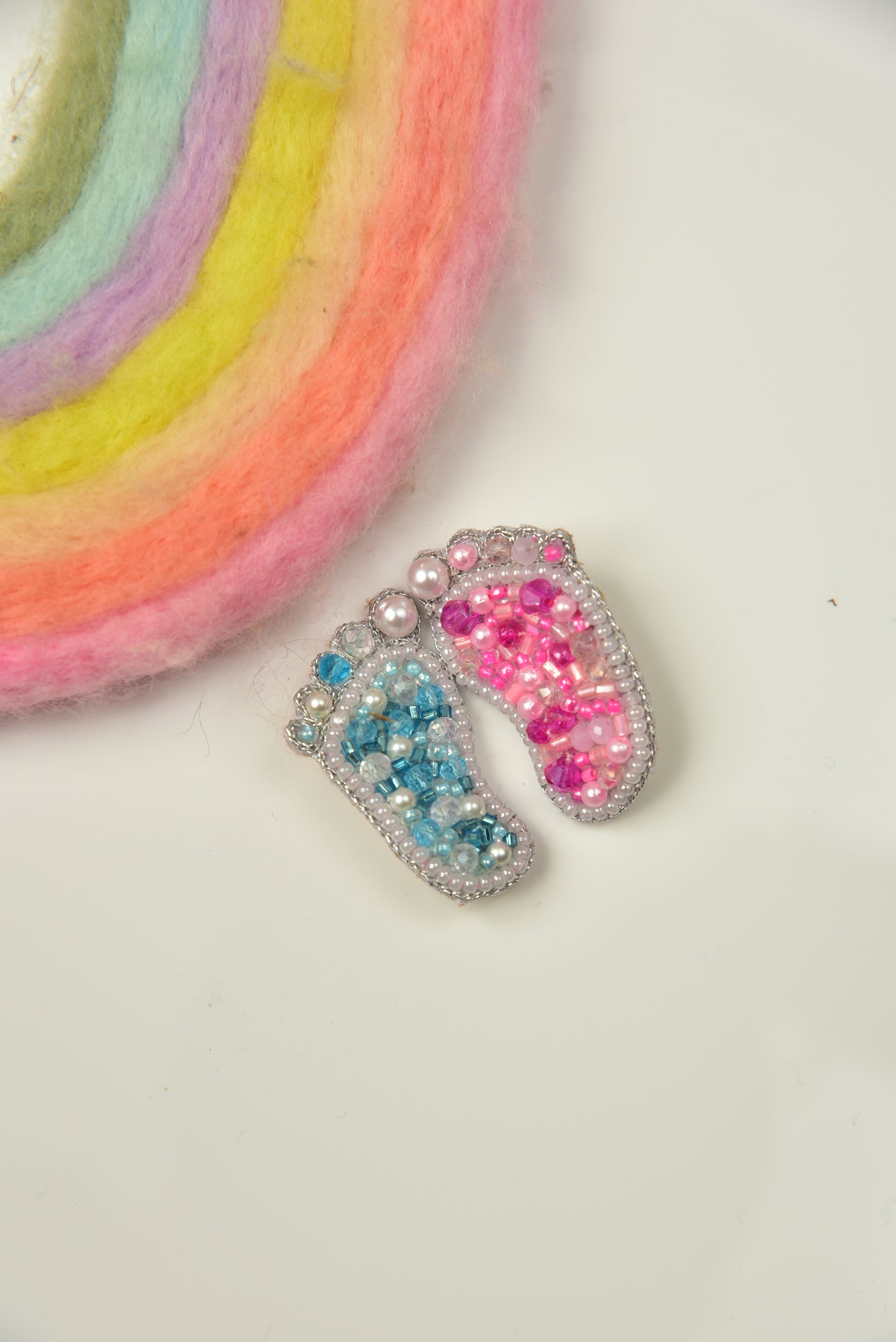 Blue and pink handcrafted baby feet brooches styled with rainbow prop—gender reveal gift set by Little Pink Llama