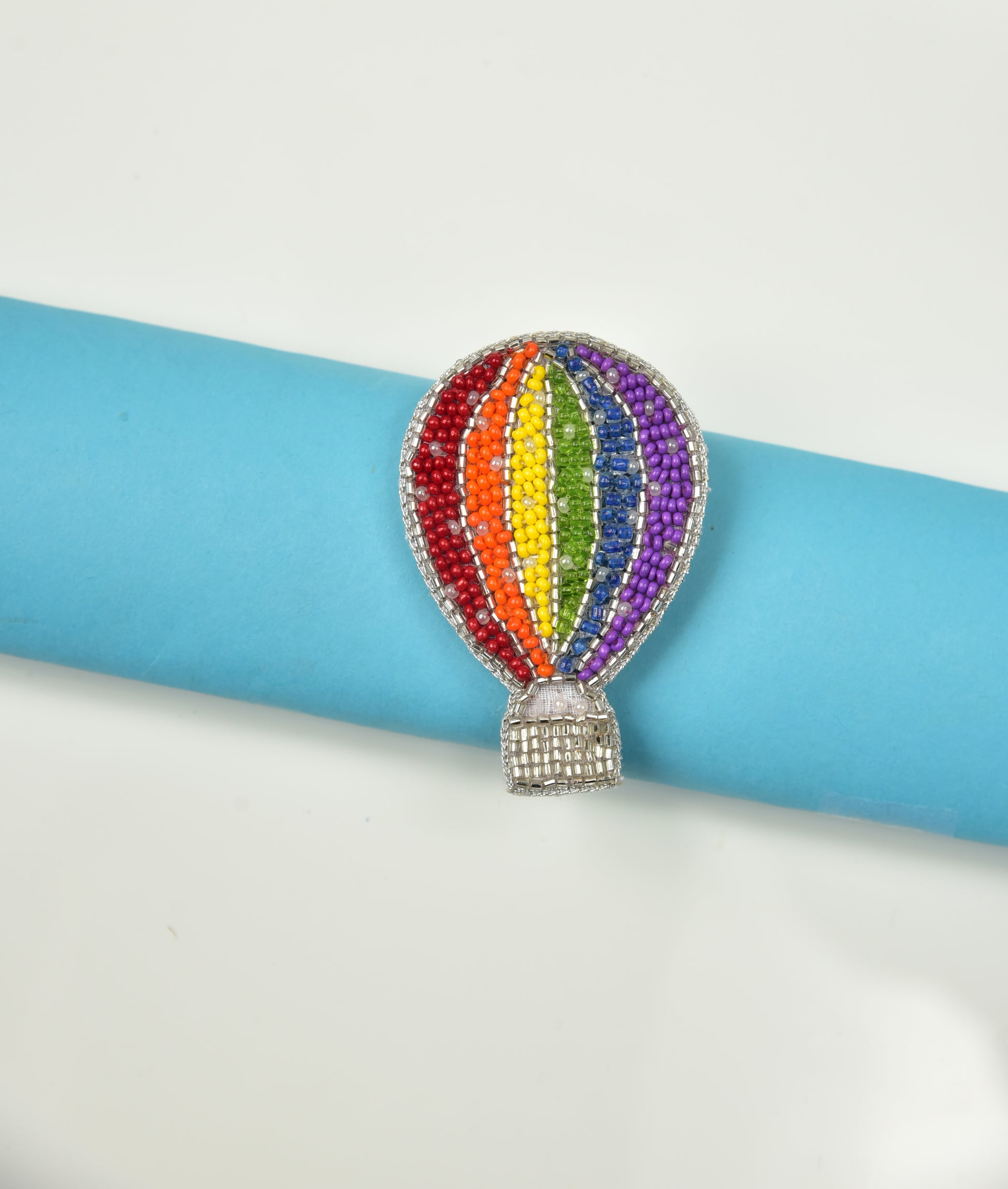 Rainbow hot air balloon brooch with multicolour beads pinned on a blue cylindrical object on white surface