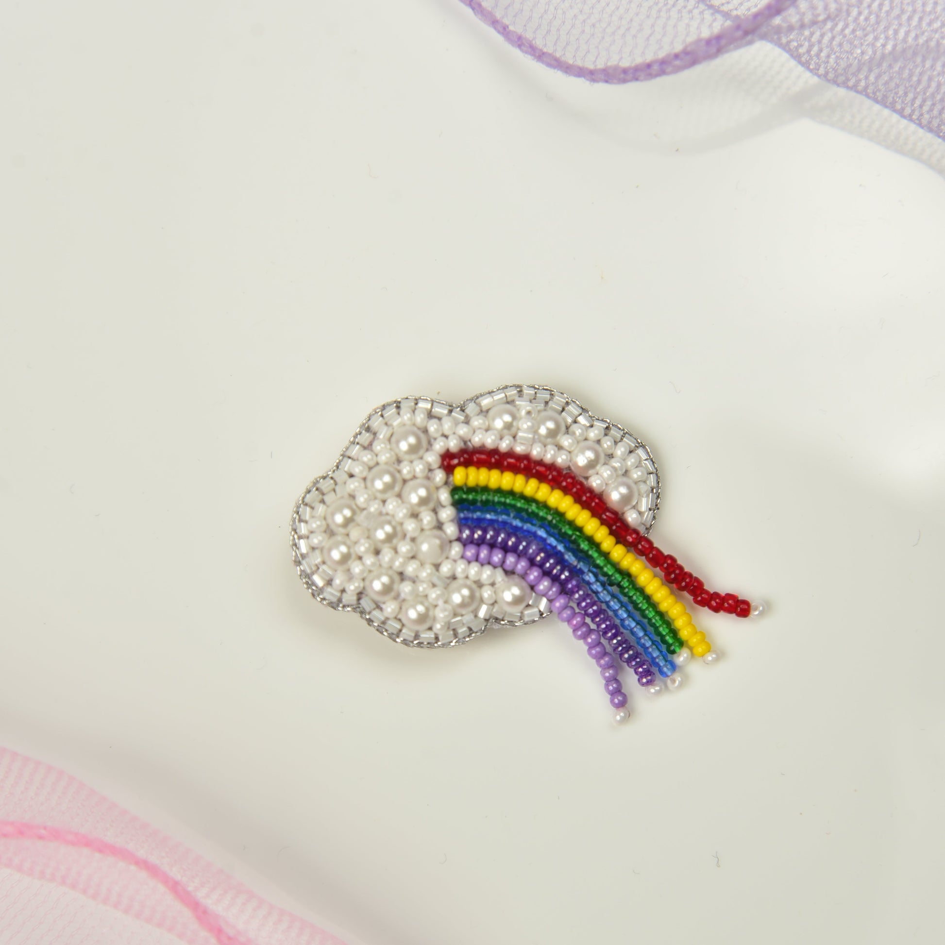 Rainbow cloud brooch pinned on white fabric - handcrafted pearl and beaded kids jewelry by Little Pink Llama