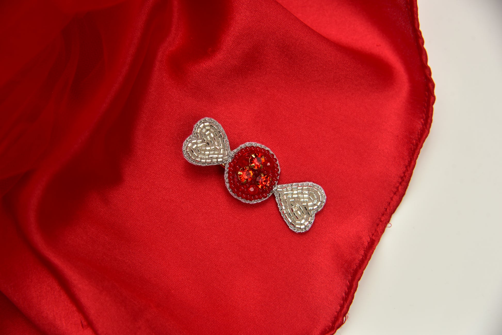 Handmade candy brooch with silver rhinestone bow wings and red gemstone center on red fabric