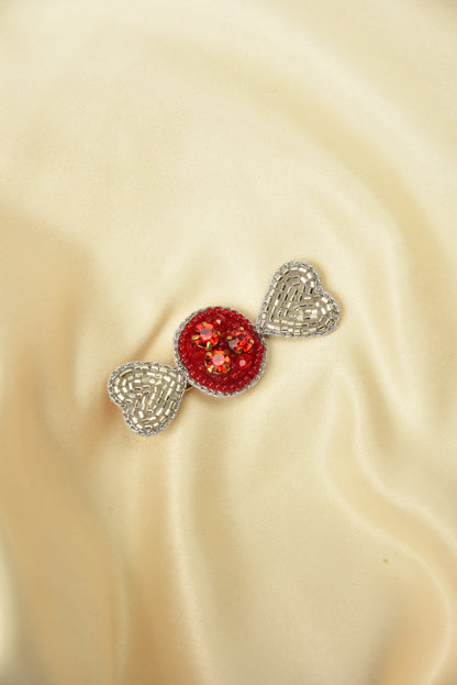 Little Pink Llama candy brooch with red gem and silver bow pinned on golden beige satin fabric