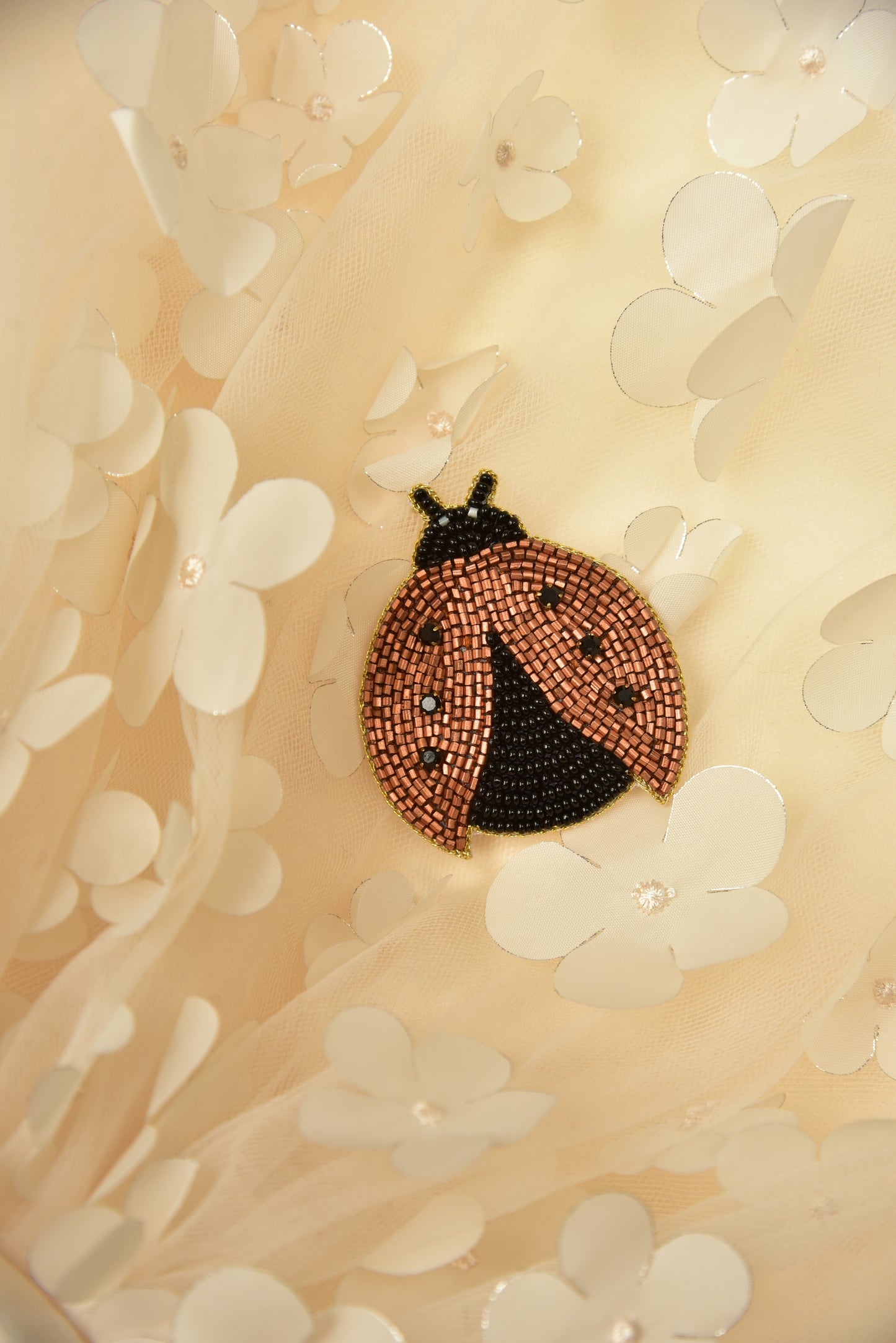 Handcrafted ladybug hair clip placed on soft floral background, showcasing elegant beaded craftsmanship
