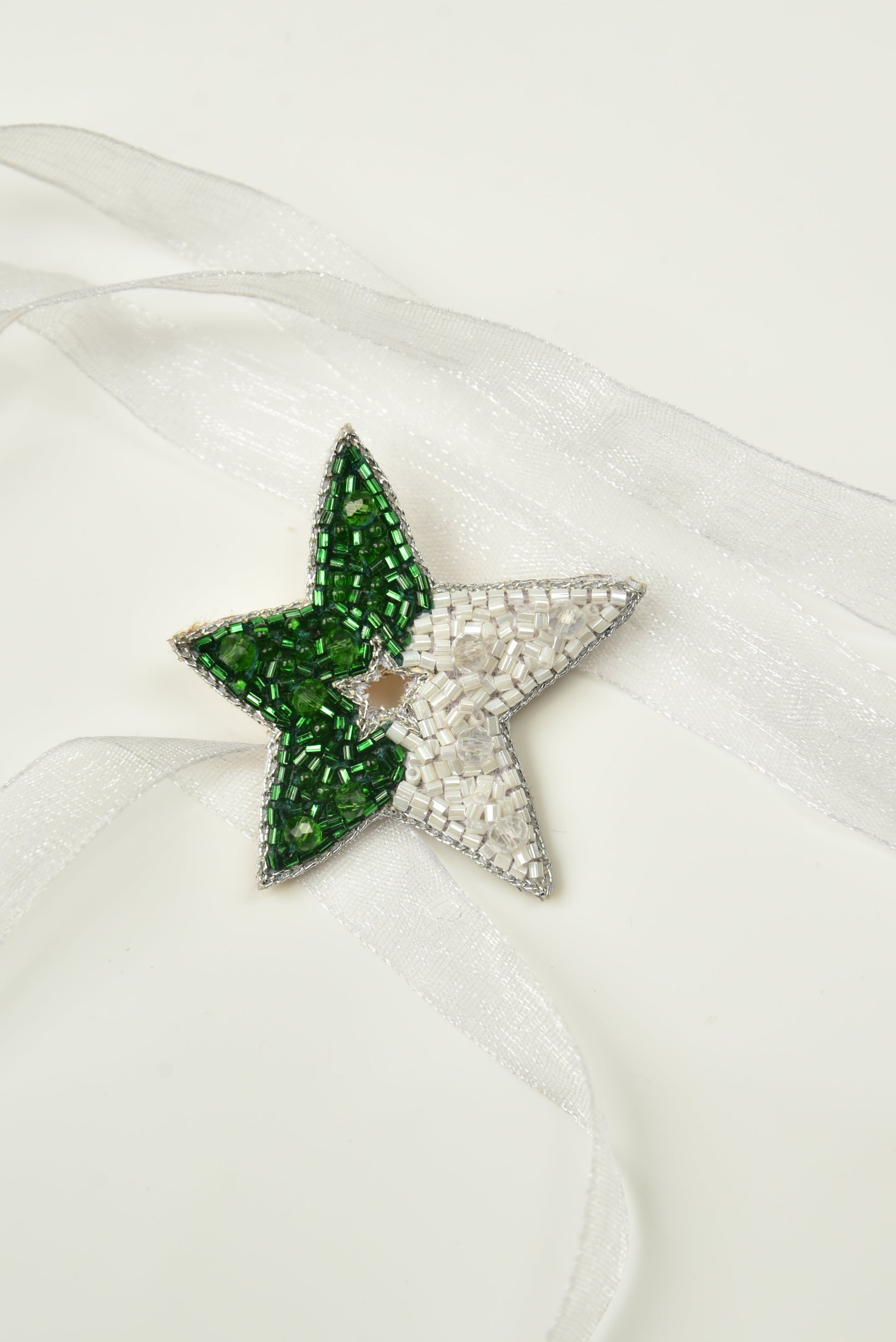 Green and white beaded Guiding Star Hair Clip on white satin fabric, close-up product shot