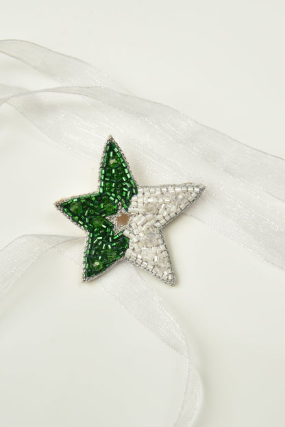 Green and white beaded Guiding Star Hair Clip on white satin fabric, close-up product shot