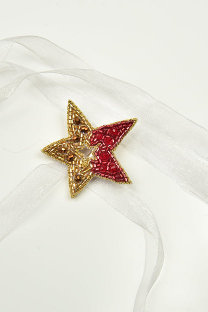 Red and gold beaded Guiding Star Hair Clip on white satin fabric, close-up product shot
