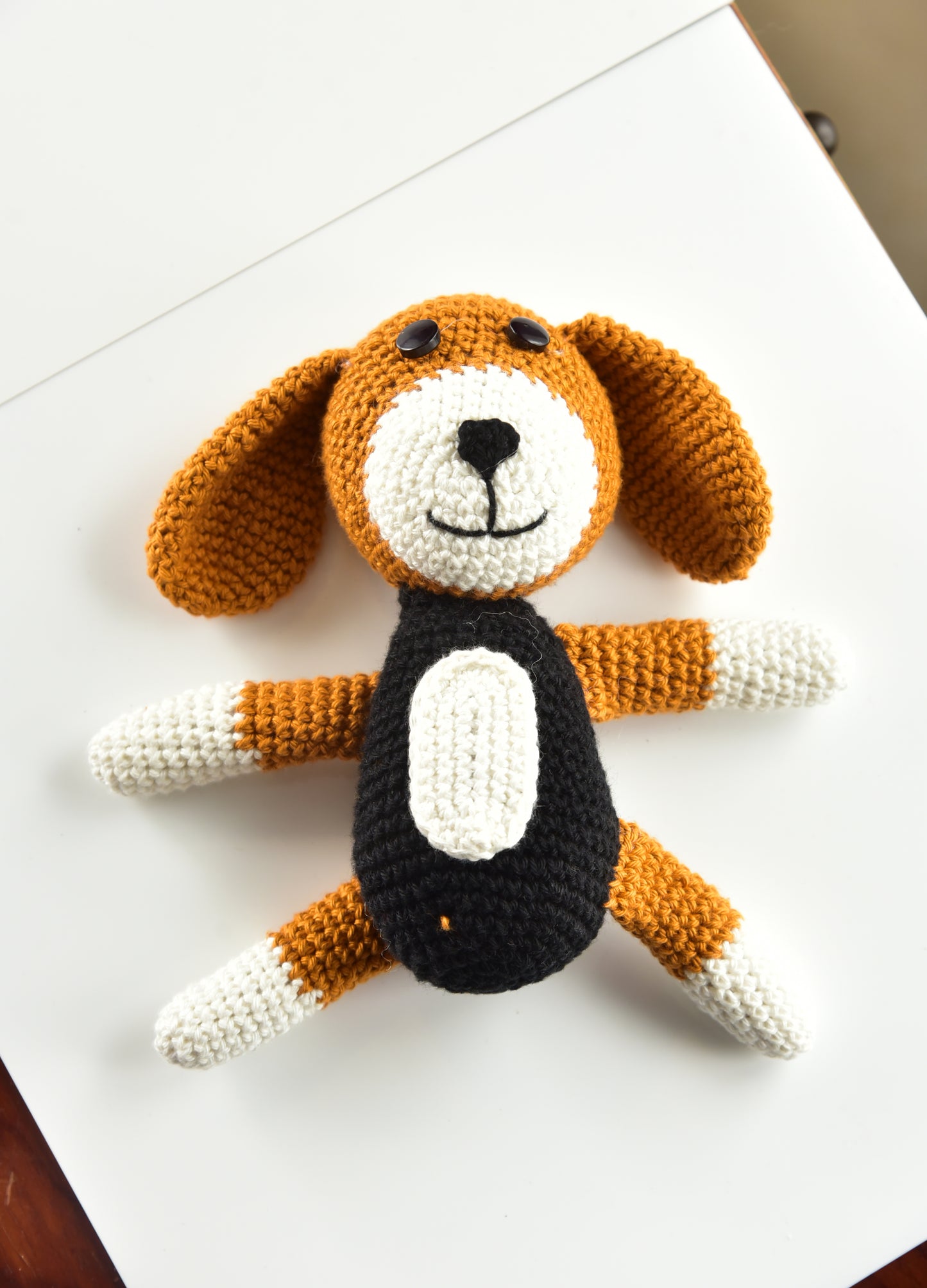 Handmade crochet dog stuffed animal in brown, black and white cotton yarn - front view on white surface