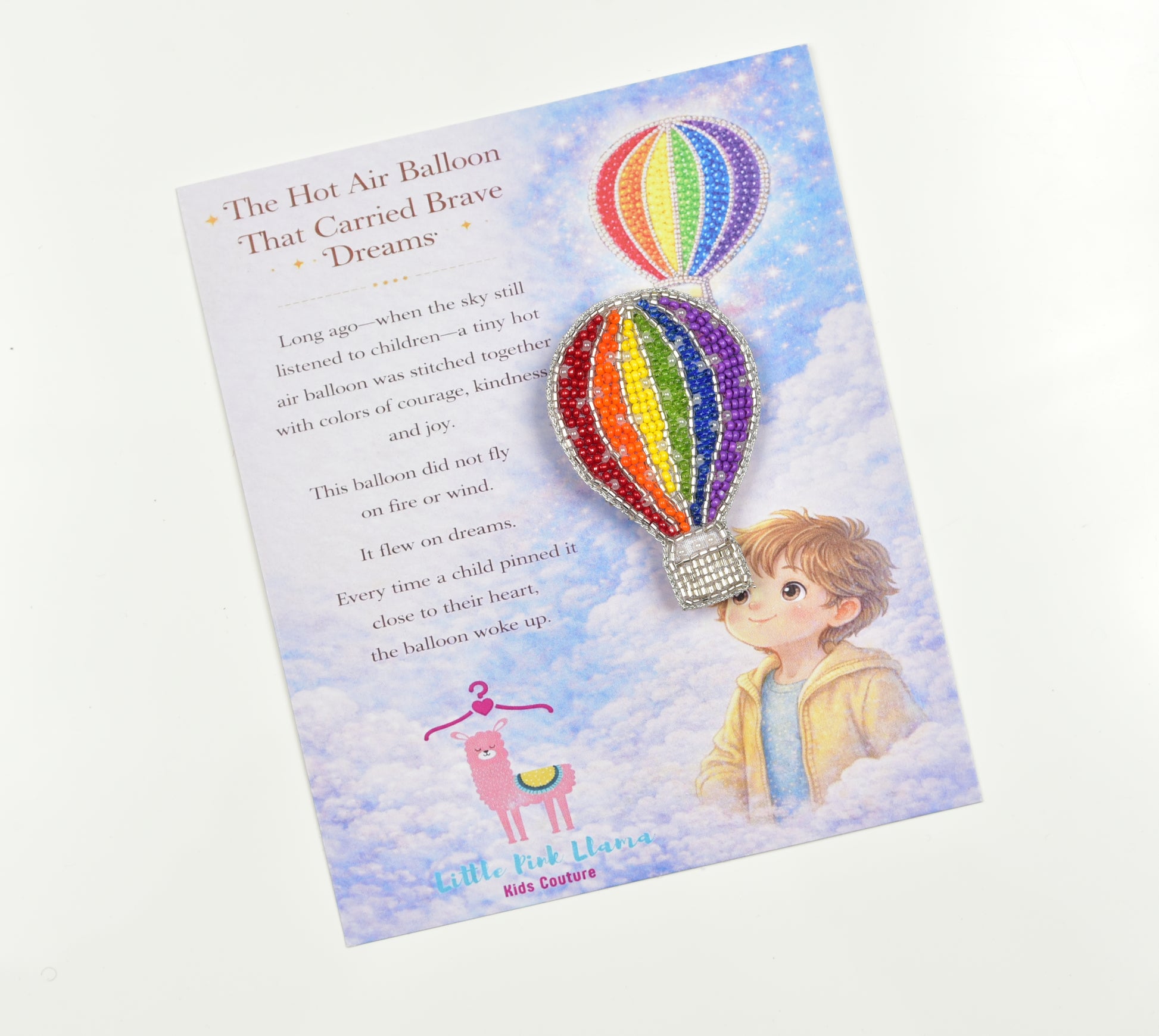 Little Pink Llama hot air balloon brooch on gift card titled The Hot Air Balloon That Carried Brave Dreams with child illustration